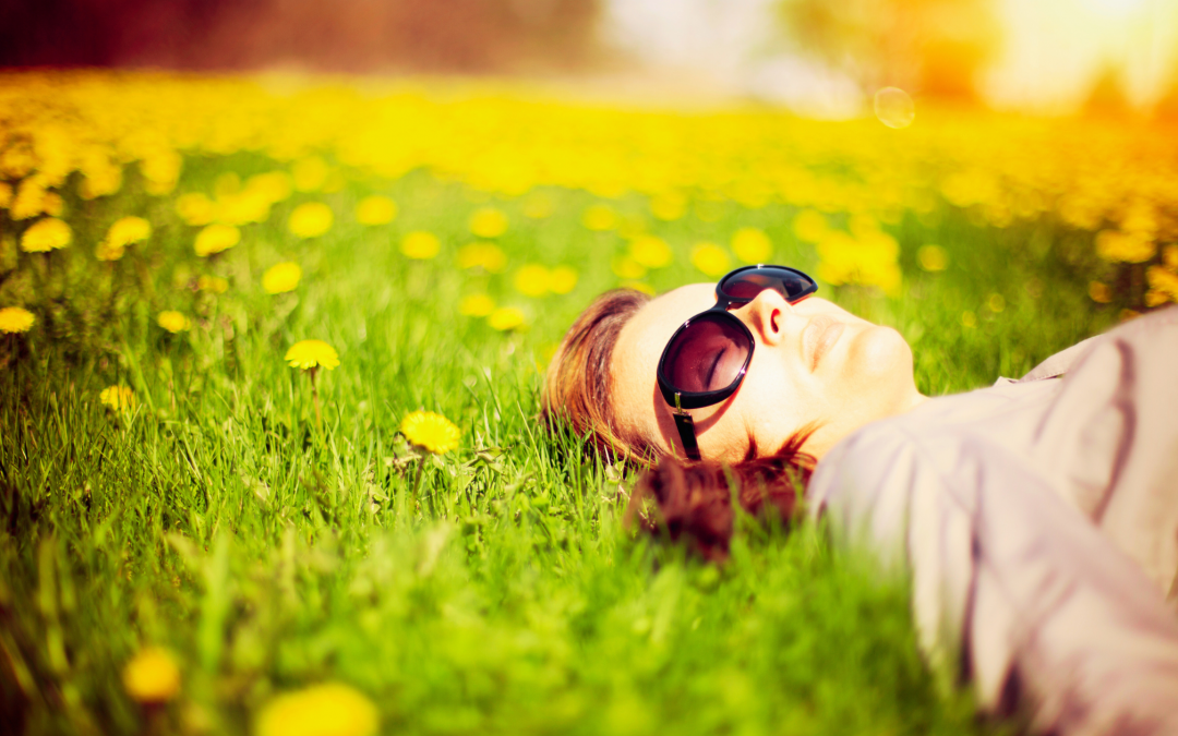 A young woman wearing sunglasses naps on a grassy field with yellow dandelions.