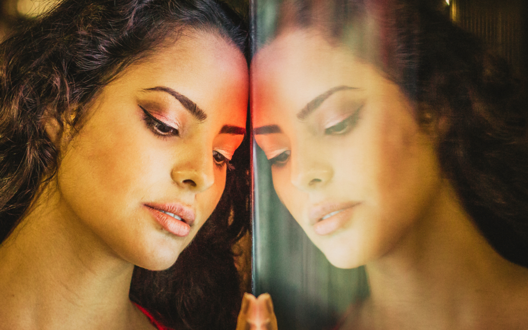 A young dark-haired woman leans against a mirror, assuming a reflective pose.