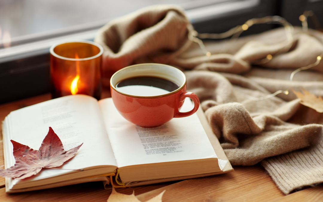 Orange cup of black coffee on open book with autumn leaves by window.