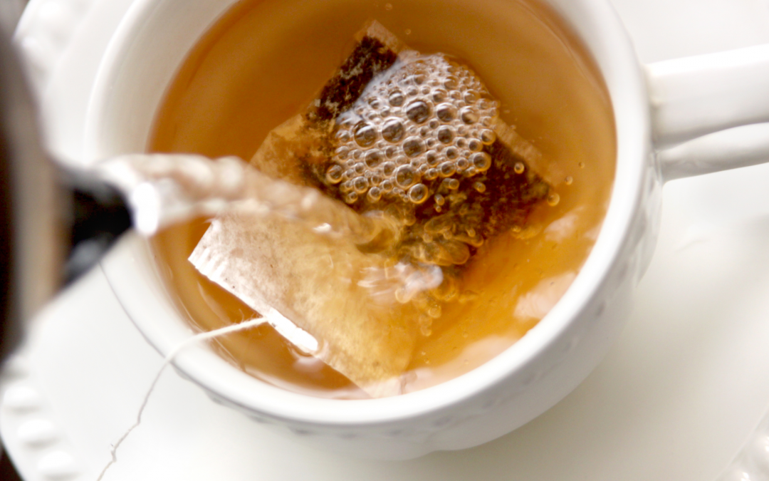 Close-up of hot water being poured from a kettle into a teacup containing a tea bag, with the water bubbling gently.