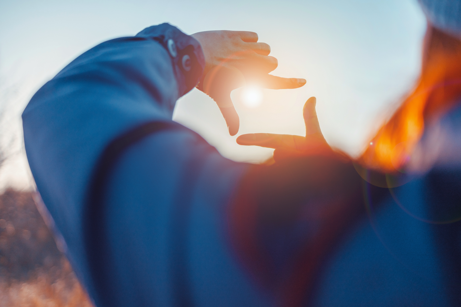 Close up of female hands making frame gesture with sunrise on an autumn meadow at sunset with sun.